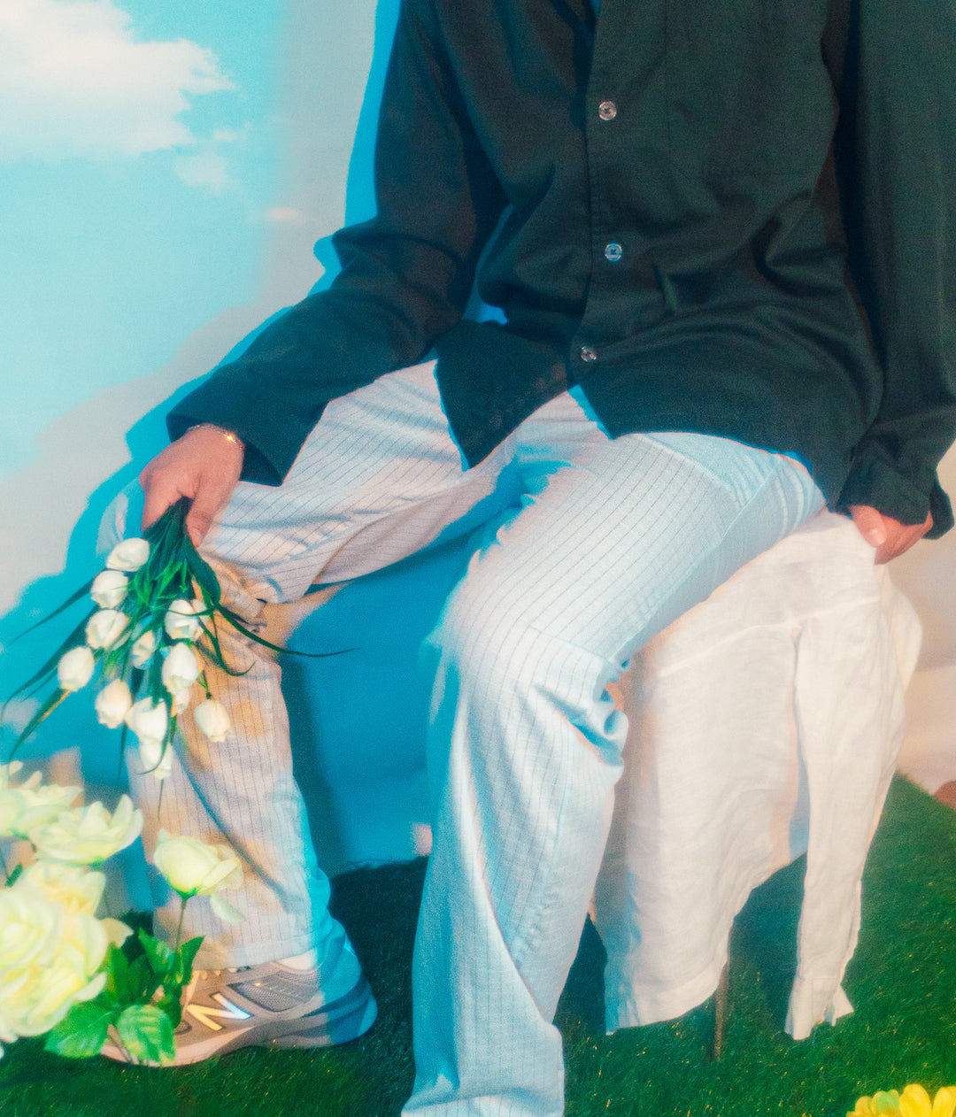 Boy sitting down wearing joujete striped pants, while holding a bouquet of tulips.